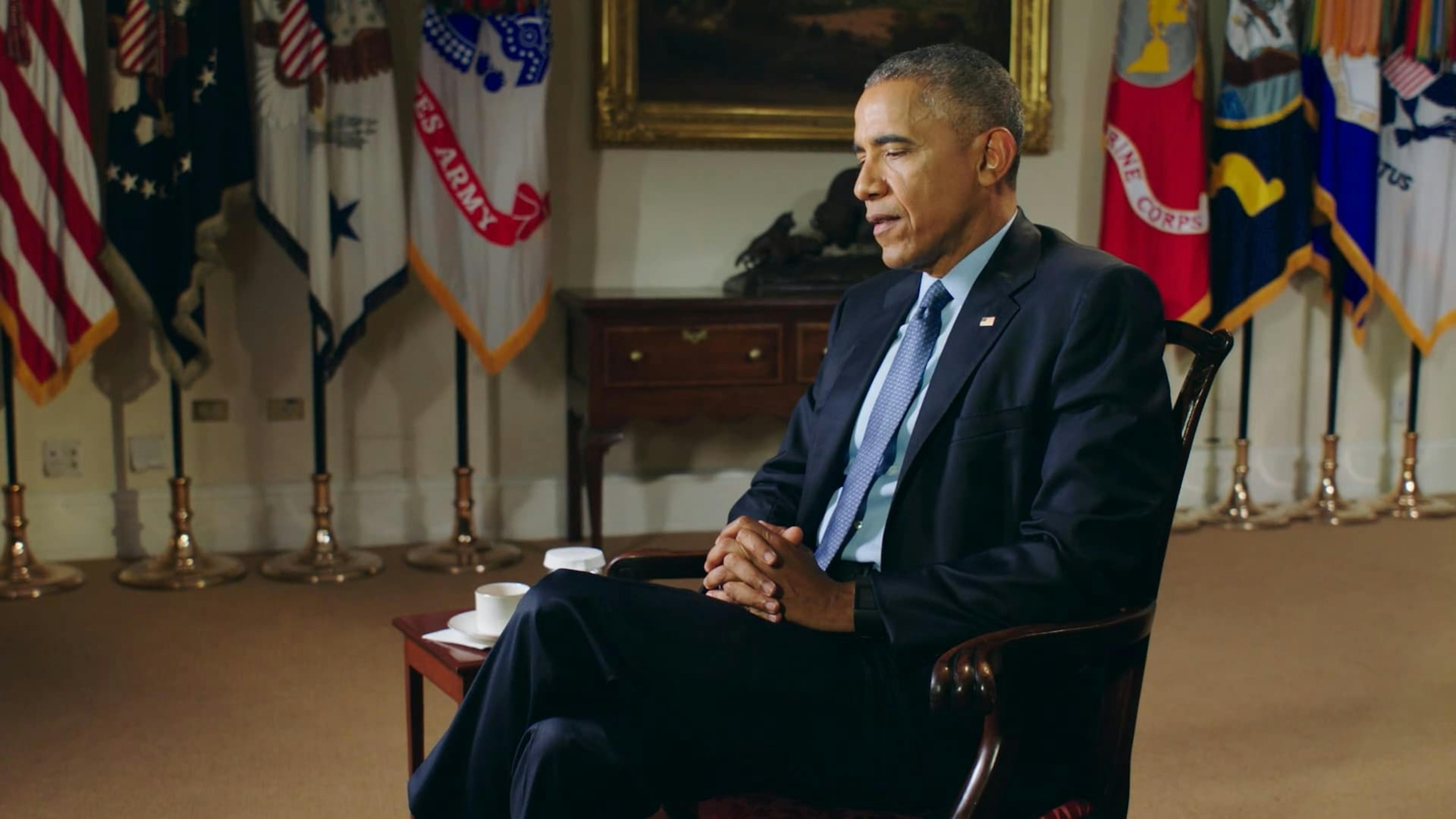 Side view of Barack Obama sat in front of flags