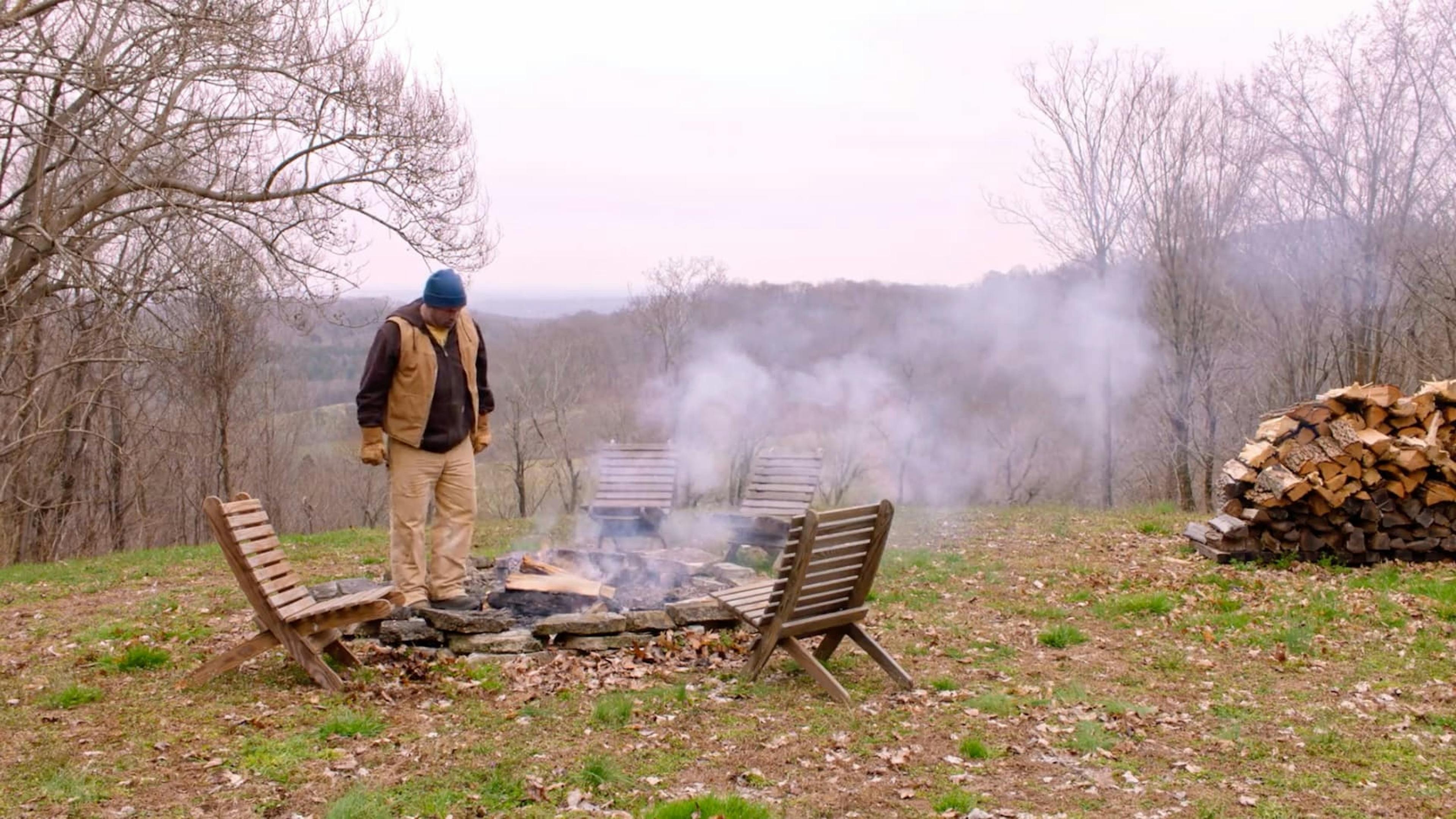 Campfire outside in daylight with man stood next to it