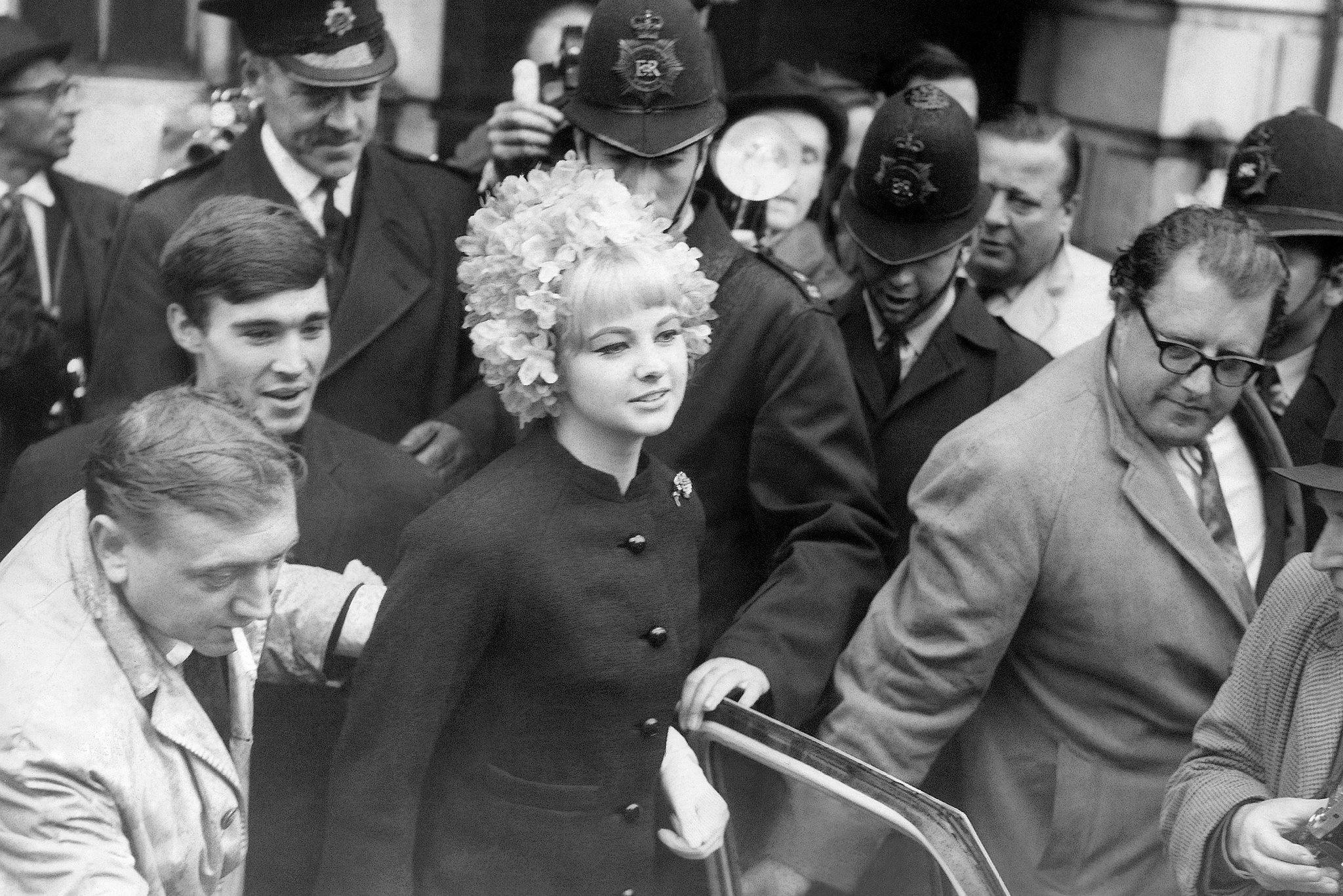 Black and white photo of woman walking surrounded by security and reporters