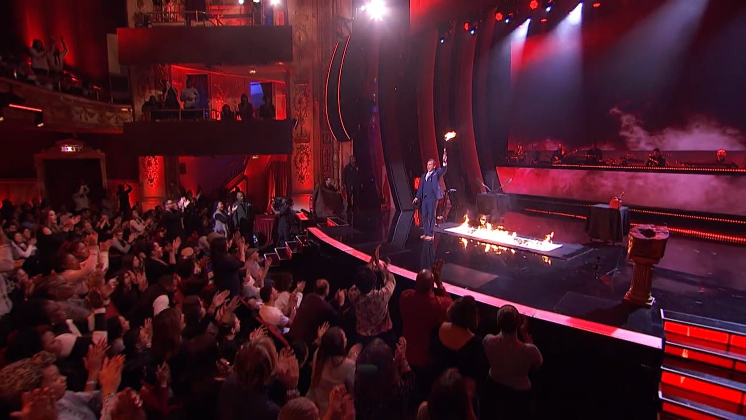 Man stood on stage with fire behind him