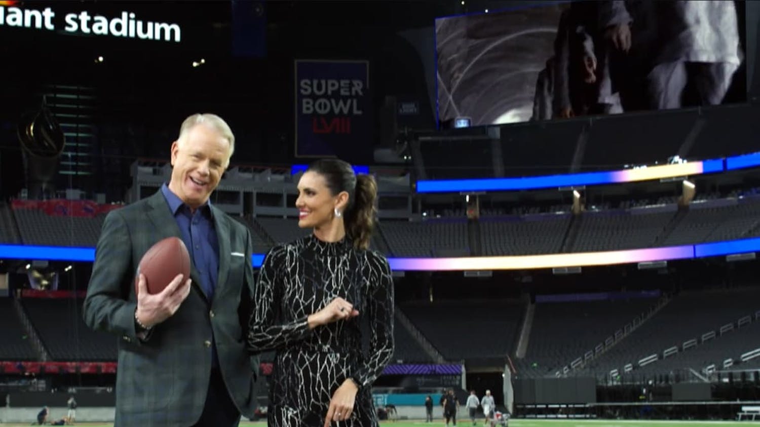 Man and woman stood on football pitch and man holding a football