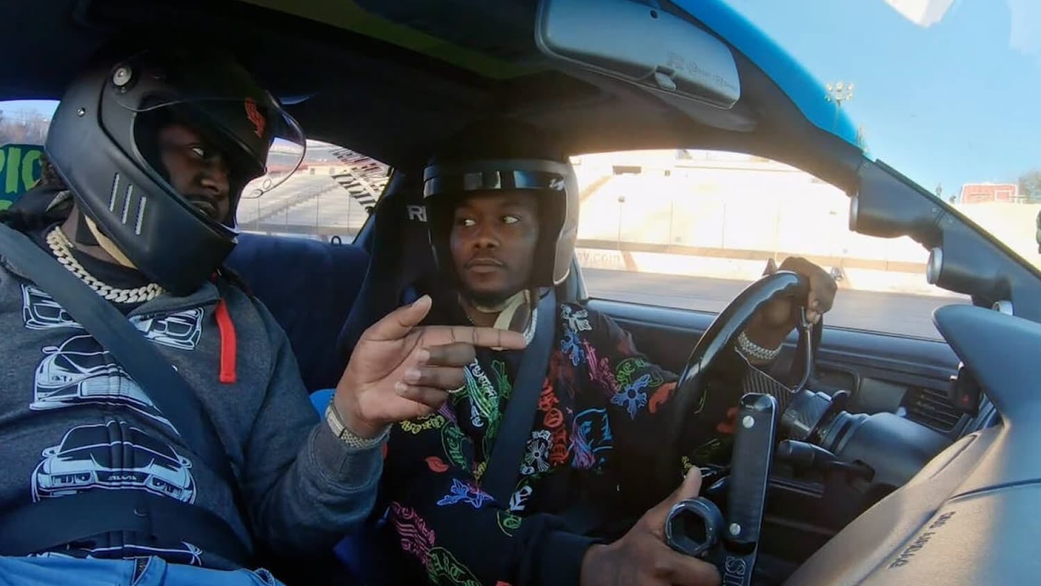 Two men wearing helmets talking in sports car