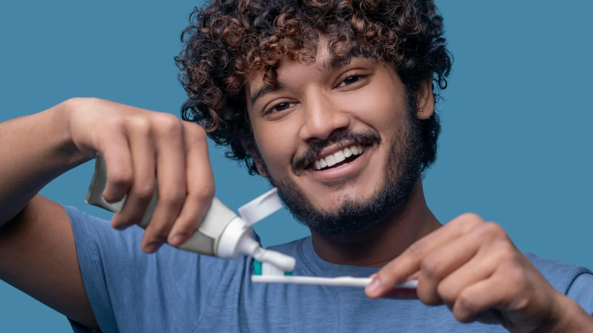homem sorridente segurando escova e pasta de dentes nas mãos