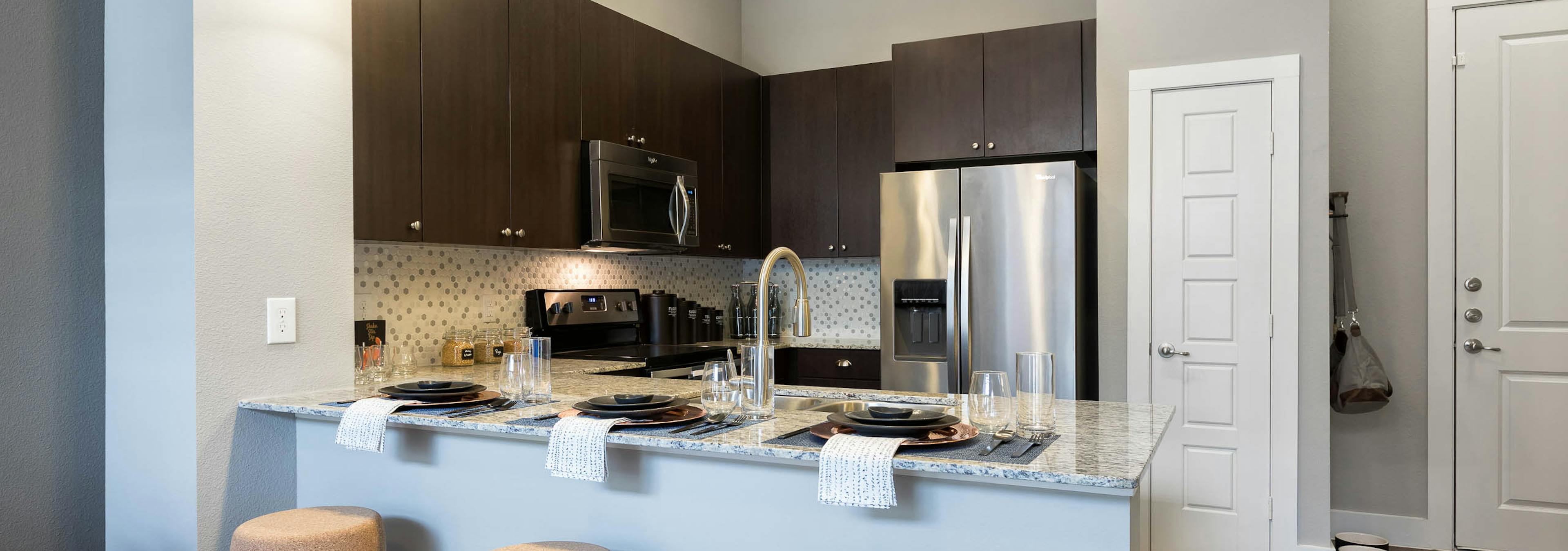 AMLI Frisco Crossing kitchen with three stools at granite countertop and tile backsplash and stainless steel appliances