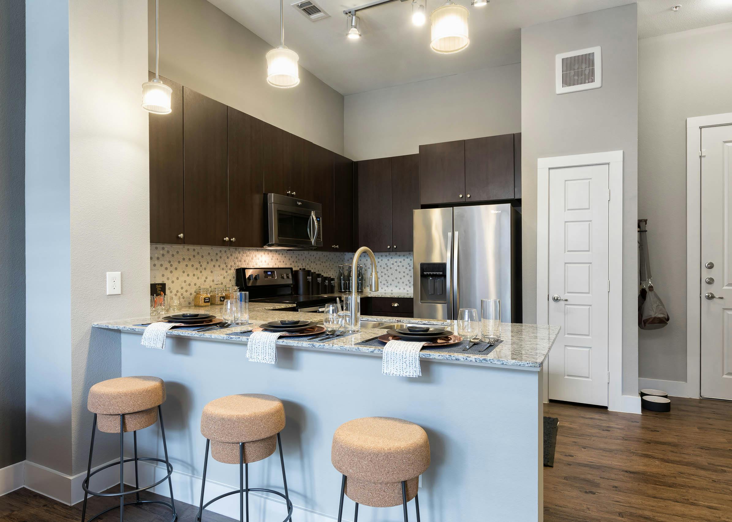 AMLI Frisco Crossing kitchen with three stools at granite countertop and tile backsplash and stainless steel appliances