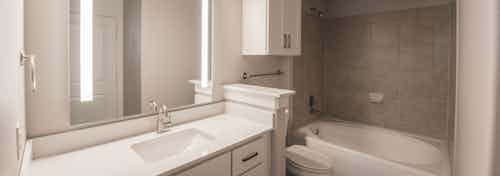 Interior view of AMLI Las Colinas apartment bathroom with granite countertop and white cabinets and oval garden tub