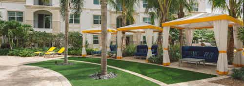 Daytime view of a poolside yard area at AMLI Sawgrass Village with flowing cabanas and palms separated by verdant landscaping