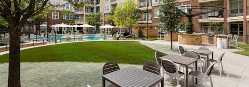 Daytime view of table and chairs near grill station at AMLI Frisco Crossing apartments with pool area in background
