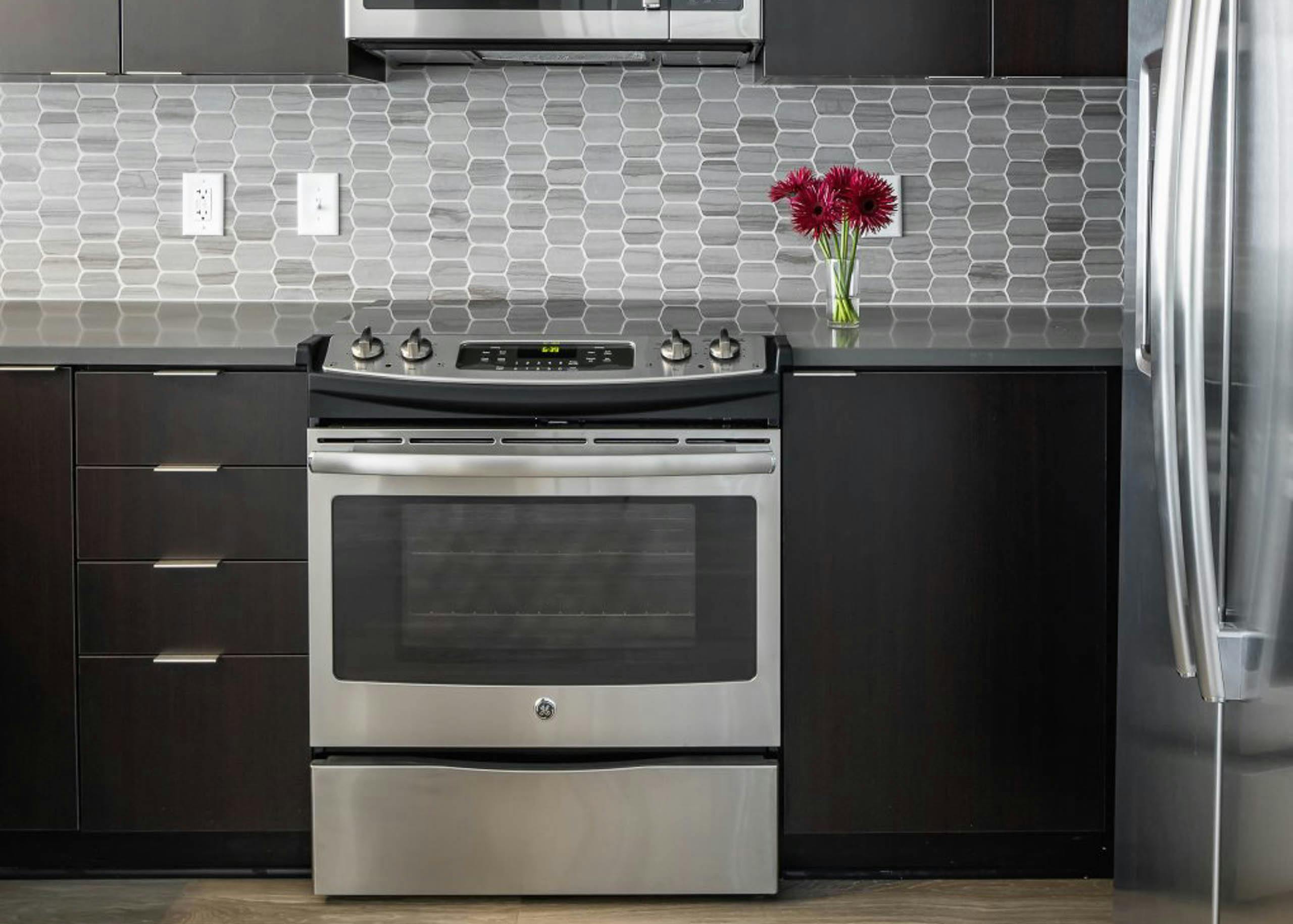 Interior of AMLI Arts Center Kitchen with black cabinets and stainless steel appliances with a grey patterned backsplash