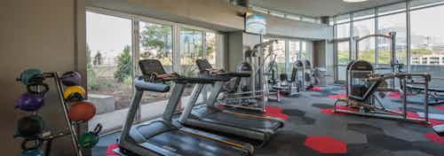Interior of fitness center at AMLI Design District apartments with cardio machines and windows overlooking roof deck