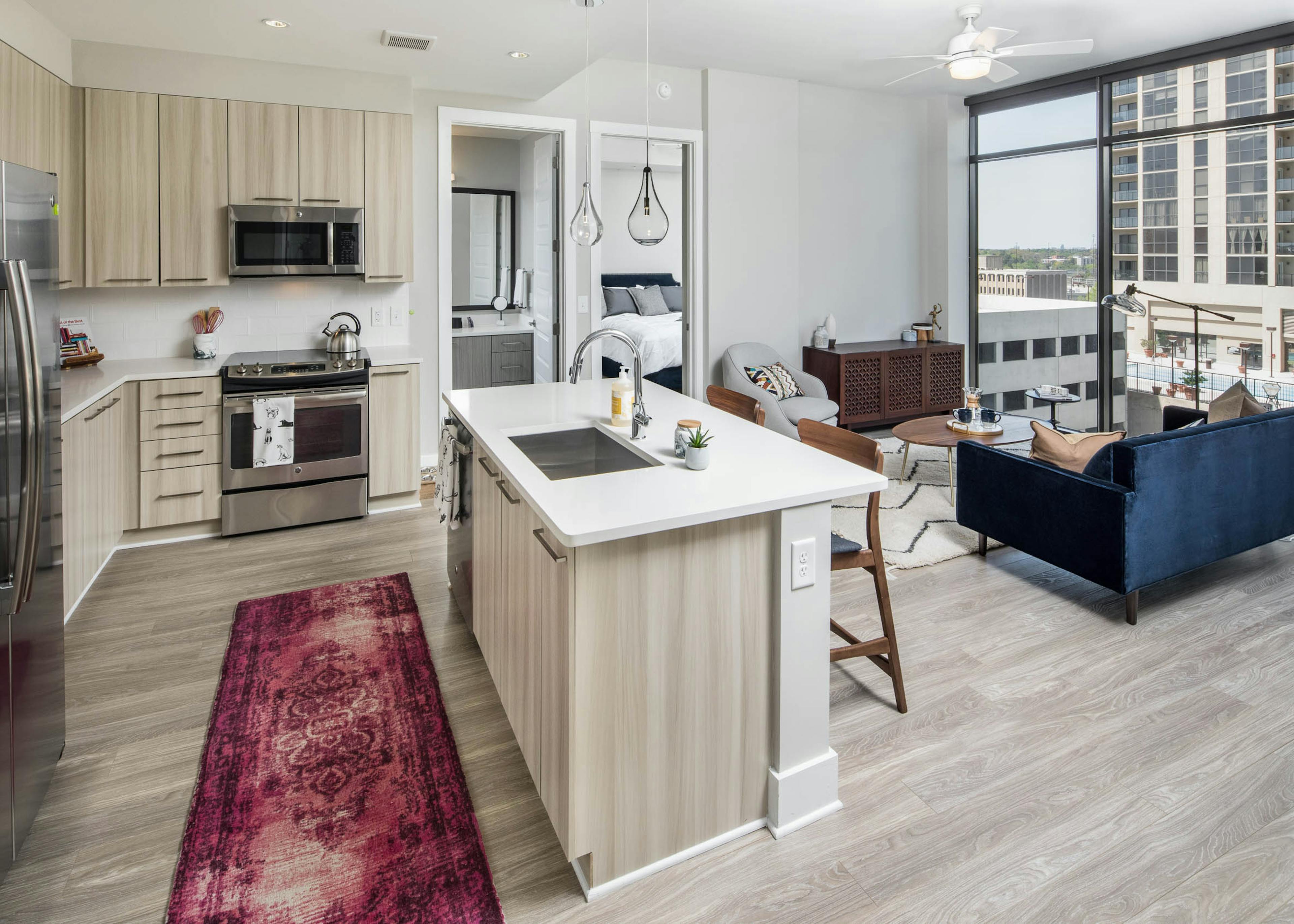 AMLI Arts Center kitchen with light wood cabinets and floors leading into living area with dark blue couch and large windows