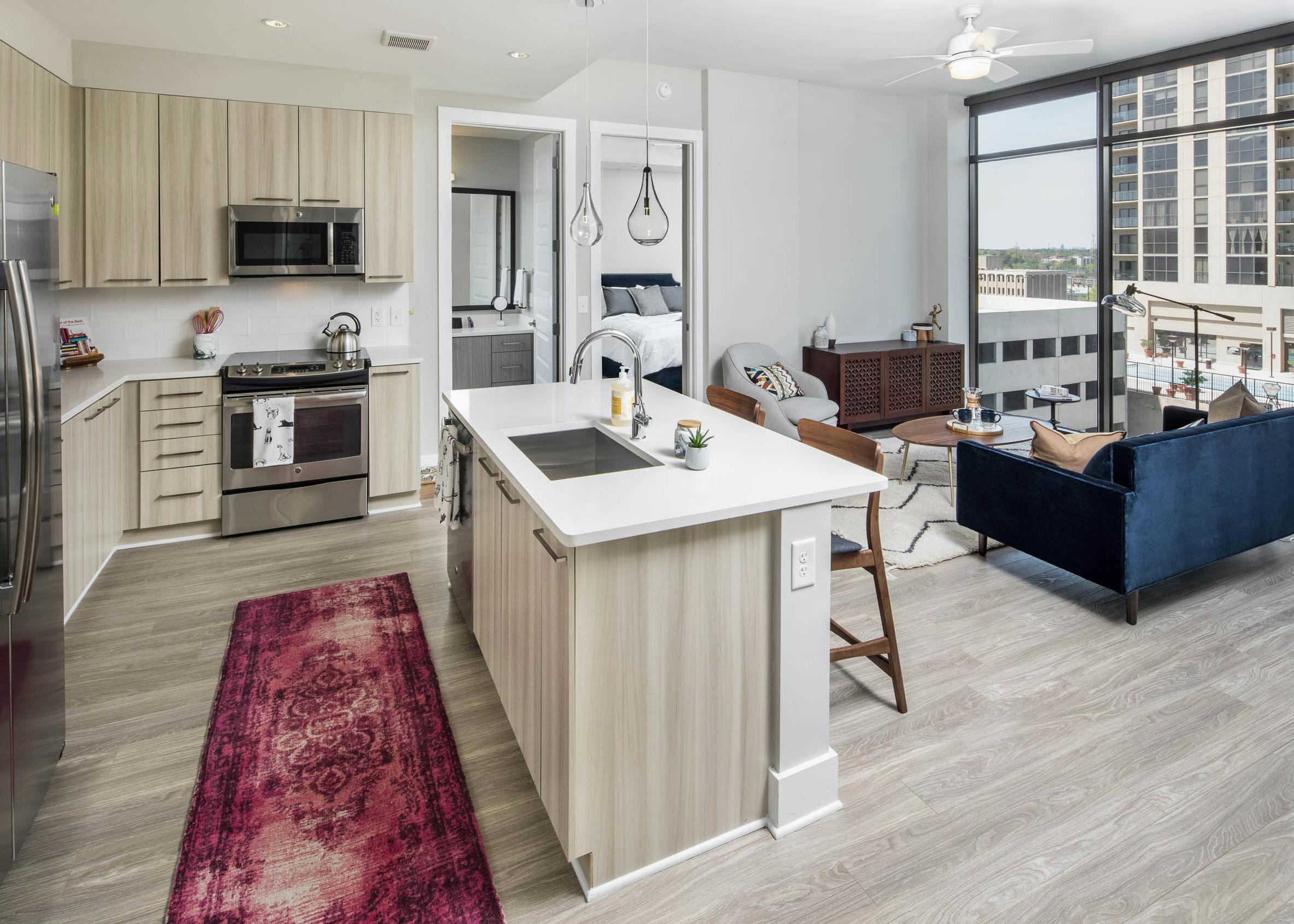 AMLI Arts Center kitchen with light wood cabinets and floors leading into living area with dark blue couch and large windows