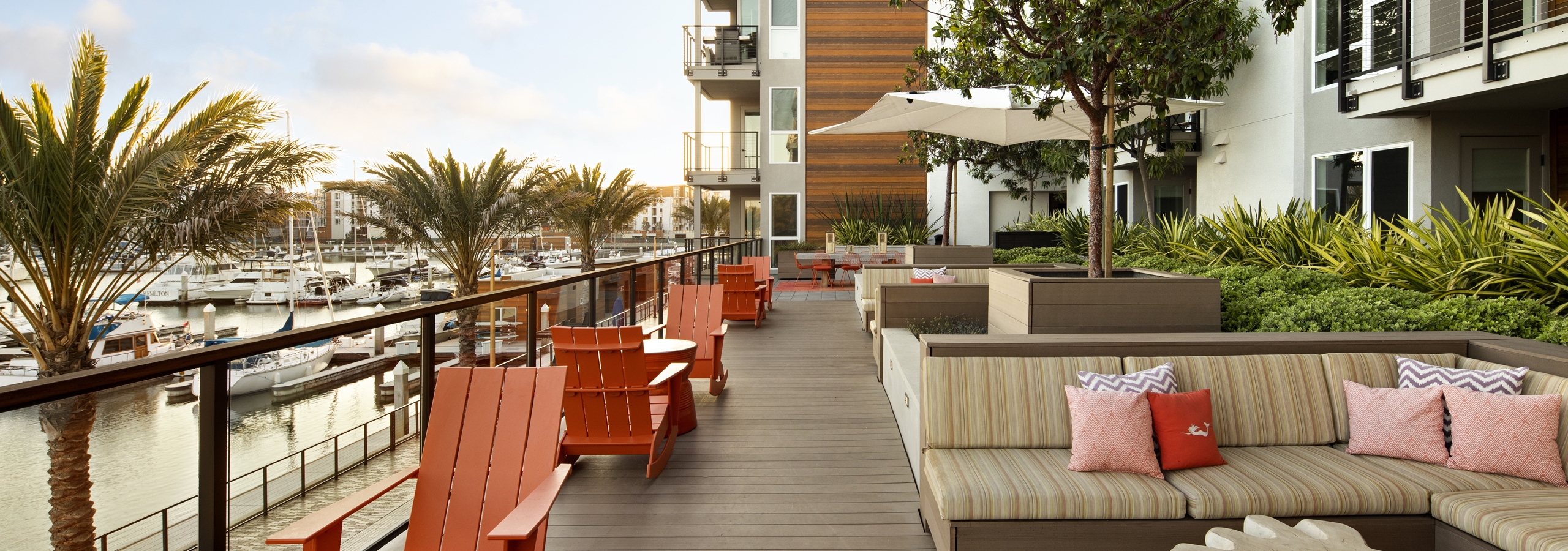 Daytime view of AMLI Marina Del Rey apartment elevated outdoor lounge with cozy seating overlooking the marina and palm trees