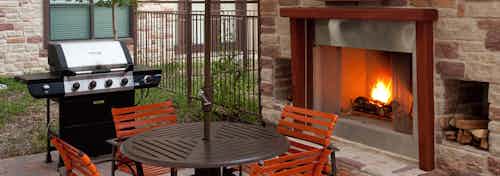 Daytime view of AMLI at Escena brick outdoor fireplace with brown table and four orange chairs and grill
