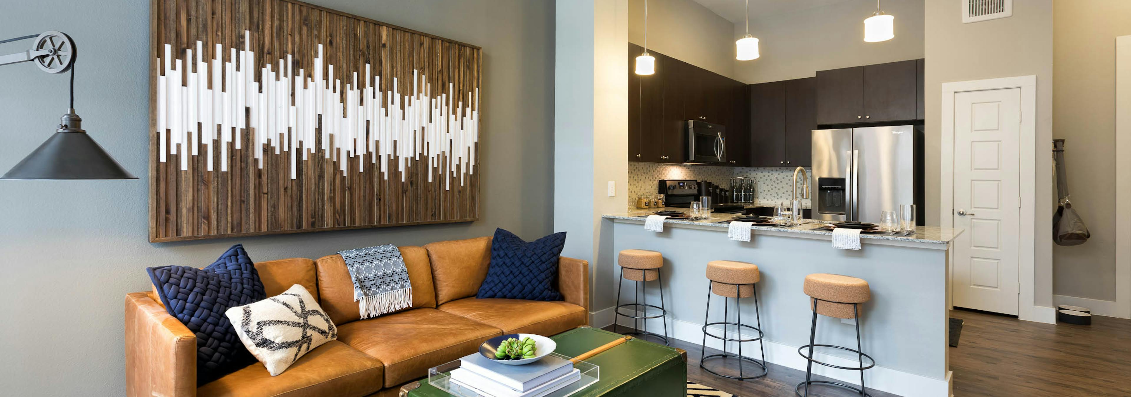 Interior view of AMLI Frisco Crossing apartment kitchen with stainless steel appliances and living room with couch and table