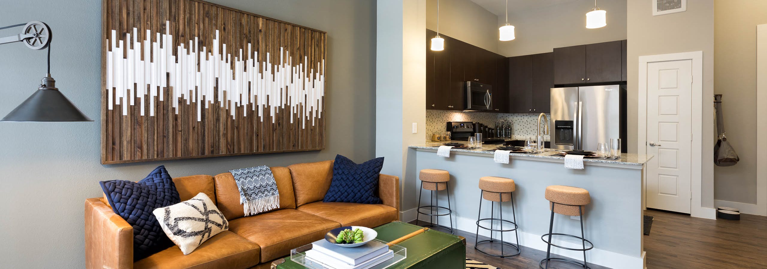 Interior view of AMLI Frisco Crossing apartment kitchen with stainless steel appliances and living room with couch and table
