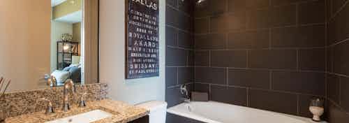 Interior view of AMLI Design District apartment bathroom with granite countertop and oval garden tub with tile surround