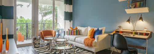 An apartment living room at AMLI Sawgrass Village with large patio doors, a couch with colorful pillows and a small desk area