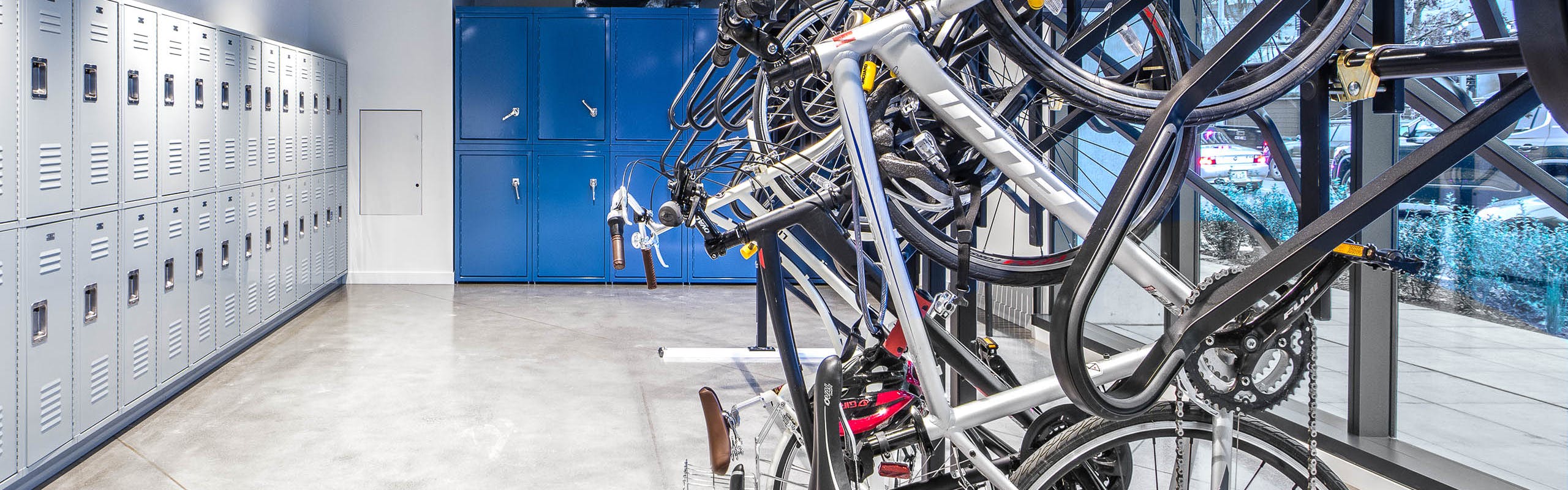 Interior bike room of AMLI Arc with bike storage tools and grey and bright blue storage lockers with large floor to ceiling windows facing the sidewalk