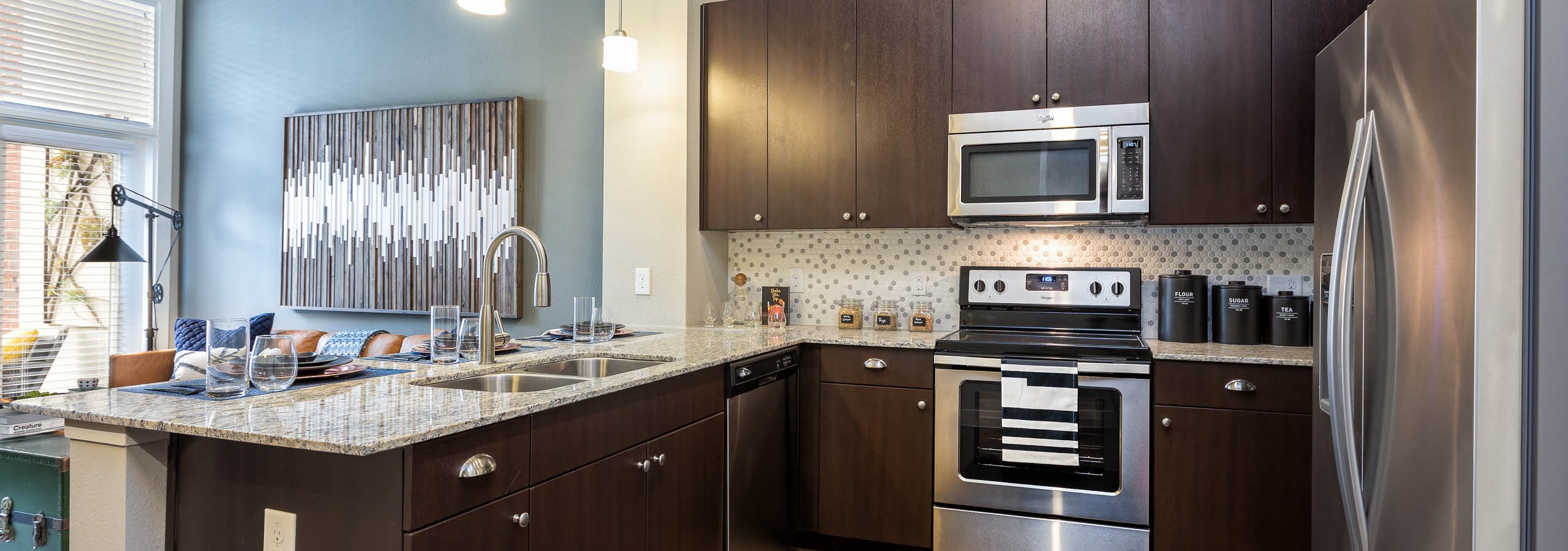 Interior of AMLI Frisco Crossing apartment kitchen with espresso cabinetry and tile backsplash and stainless steel appliances