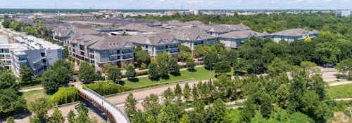 Daytime aerial view of AMLI Memorial Heights apartment building from afar with bridge and trees and highway in foreground