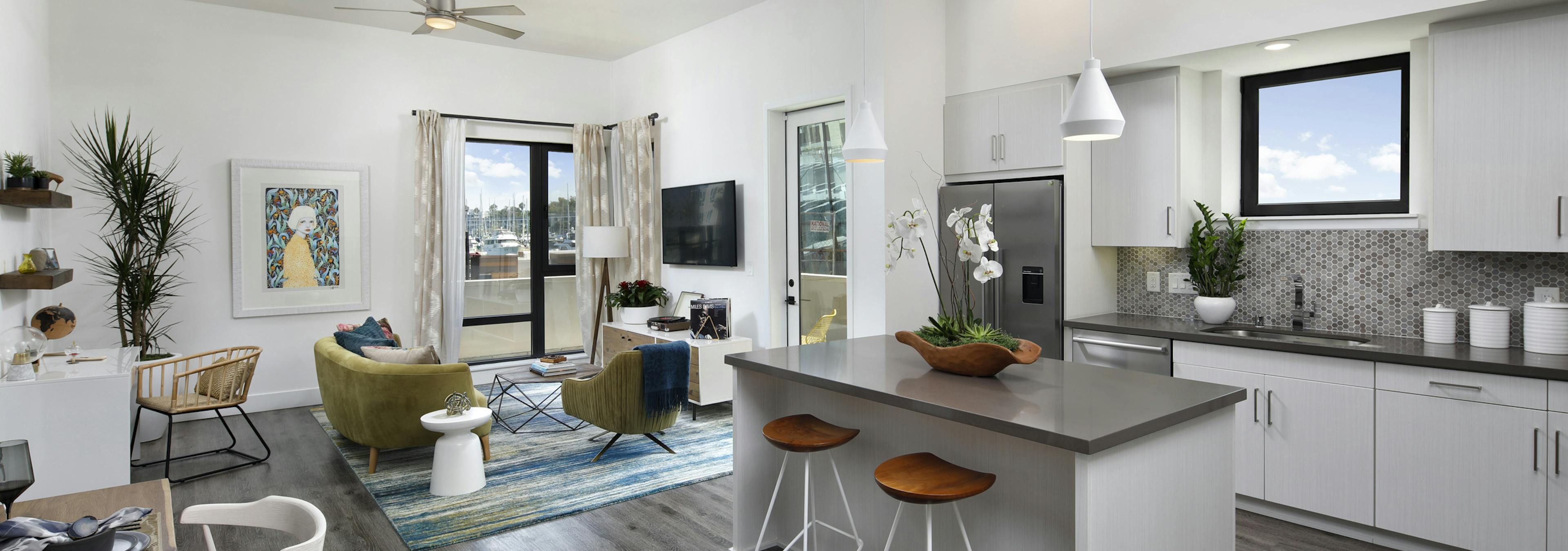 Interior of AMLI Marina Del Rey furnished apartment kitchen with white cabinetry, gray quartz countertops and living room