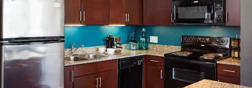 An interior view of an AMLI 900 kitchen which has teal painted walls and features dark wood cabinets and granite countertops