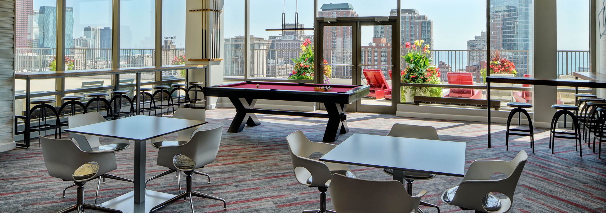 Rooftop lounge at AMLI 900 featuring tables, chairs and a pool table surrounded by glass windows with a daytime city view