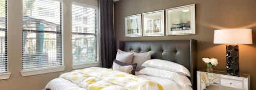 Interior view of AMLI Campion Trail apartment bedroom with bed, night stand and large windows overlooking pool courtyard