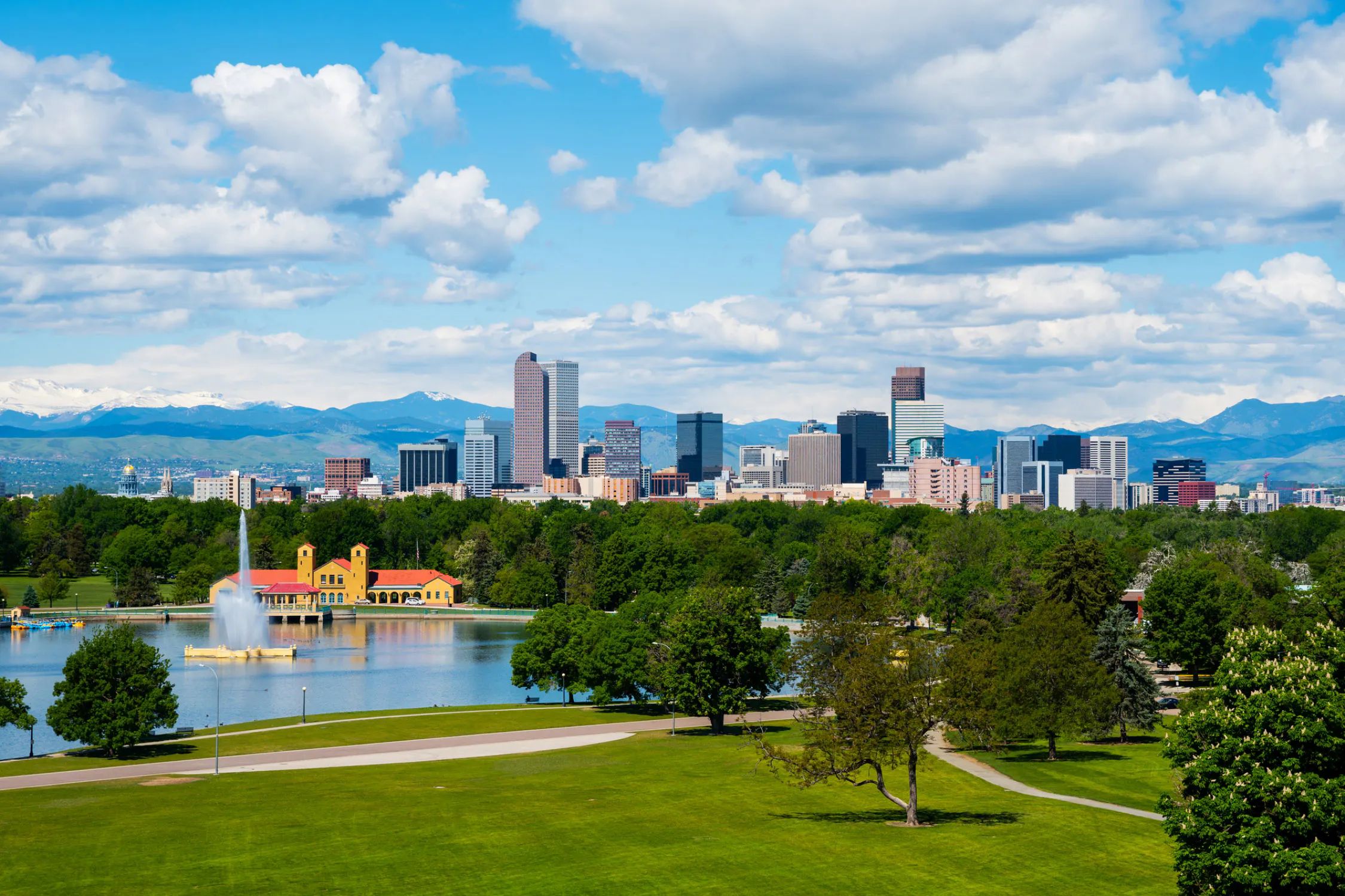 The Denver skyline set against a backdrop of the Front Range mountains on a sunny day with clouds dotting the sky