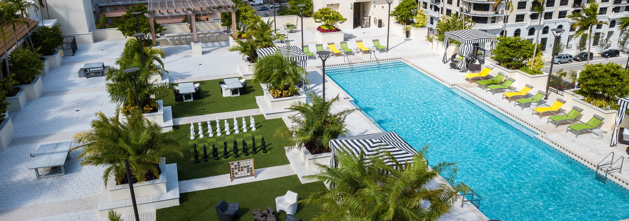 Exterior Rooftop view of the AMLI Dadeland pool with black and white striped cabanas life size chess game and pool furniture