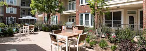 Daytime view of grill station at AMLI Frisco Crossing apartments with seating and surrounding trees, shrubs and flowers