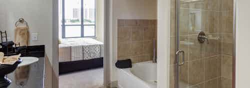Interior of AMLI Las Colinas apartment bathroom with black granite double vanity and glass shower and oval garden tub