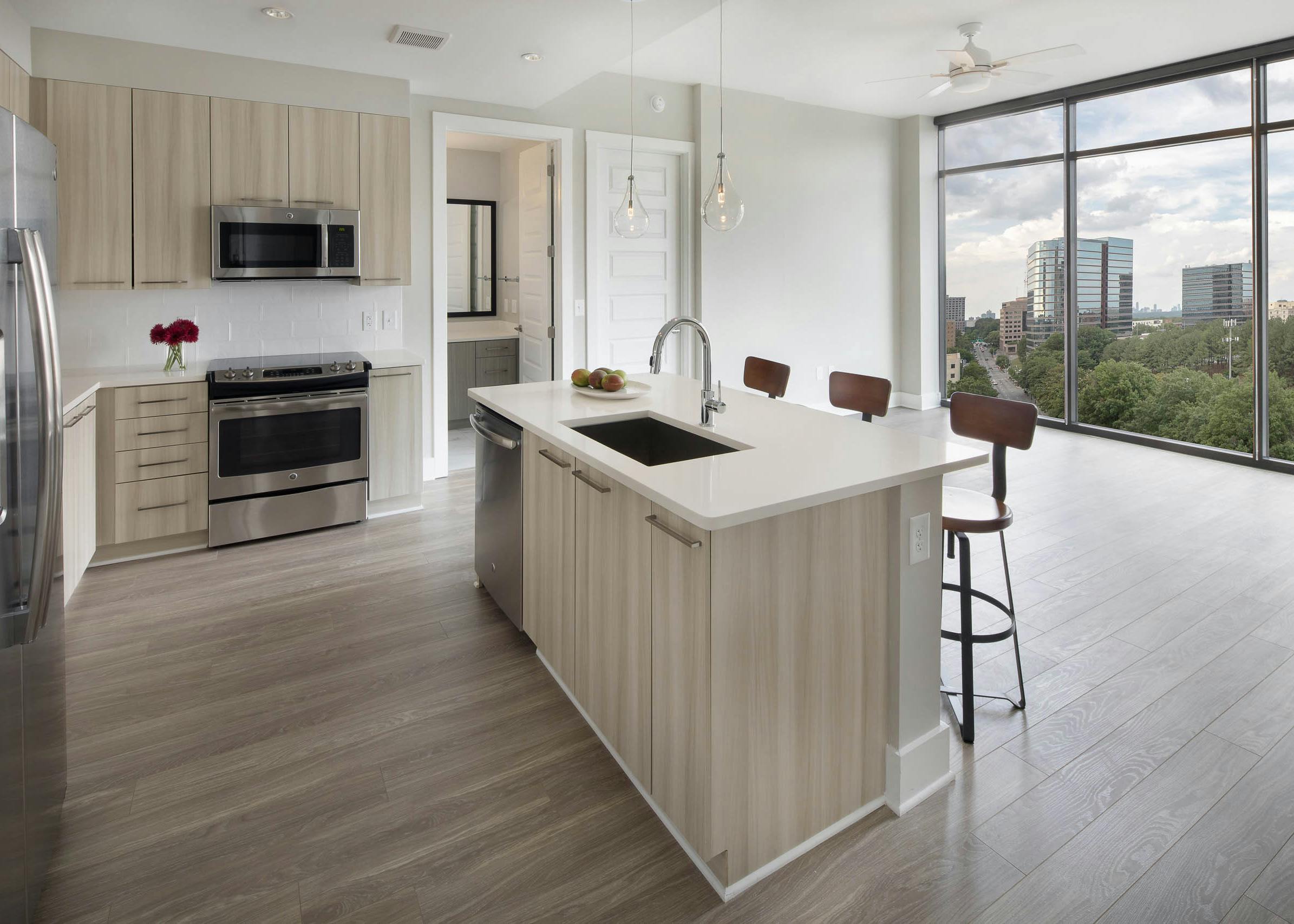AMLI Arts Center kitchen with light wood cabinets and sleek white countertops connecting to living area with large windows