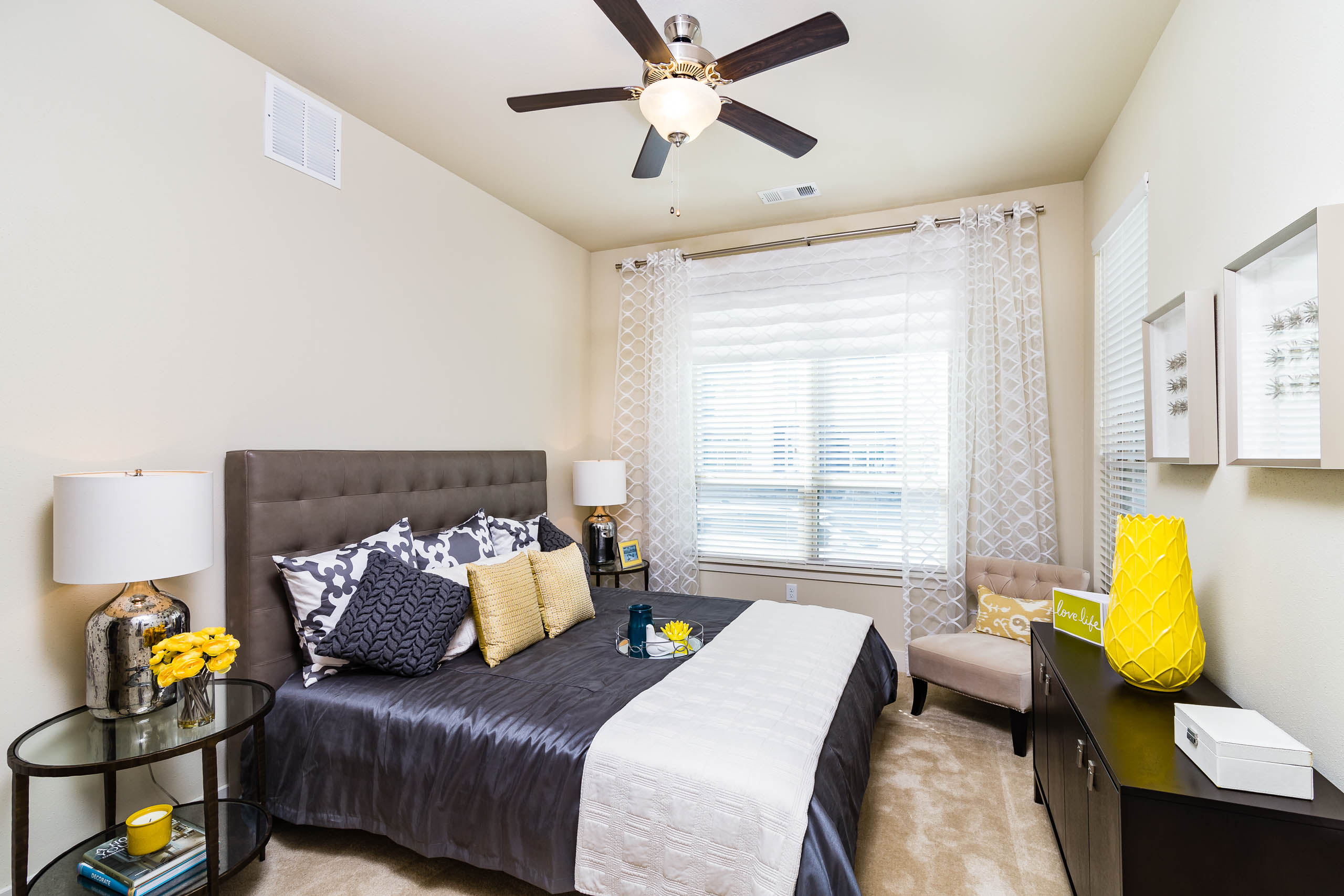 Interior view of AMLI RidgeGate bedroom with queen bed and gray upholstered headboard facing large window with sheer curtains