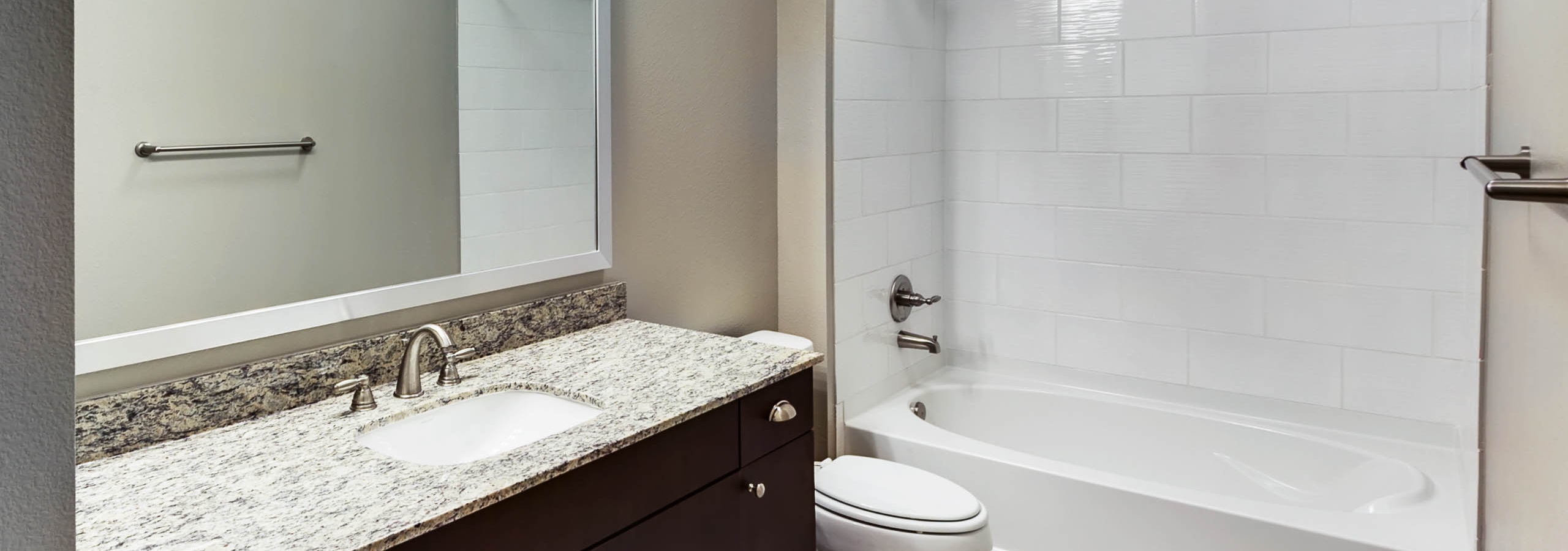 Interior view of AMLI Frisco Crossing apartment bathroom with granite countertop and espresso cabinets and oval garden tub