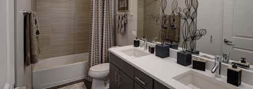 Interior view of bathroom at AMLI Lofts containing a double vanity, toilet and bathtub with a striped curtain and beige tiles