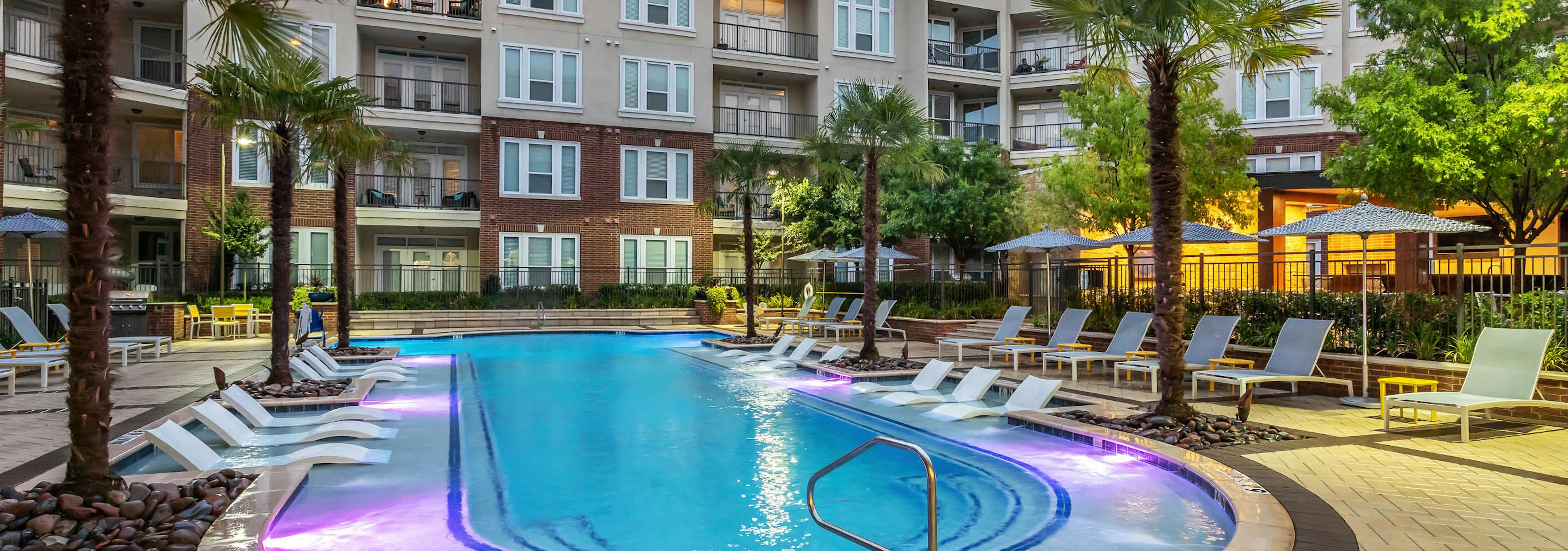 Dusk view of AMLI Frisco Crossing pool surrounded by lounge seating and palm trees