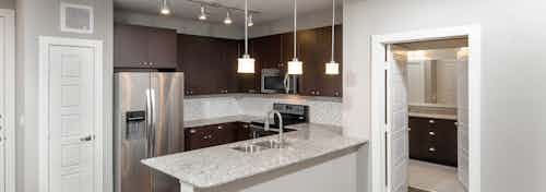 Interior of AMLI Frisco Crossing apartment kitchen with espresso cabinetry and tile backsplash and stainless steel appliances