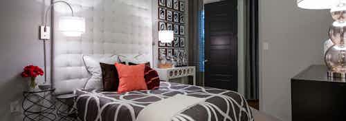 AMLI Uptown apartment bedroom with bed, white cushioned wall, unique nightstands and overhead lamps and tall window