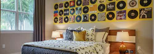 Interior view of an AMLI Sawgrass Village apartment bedroom with a bed underneath wall art made from vinyl record albums
