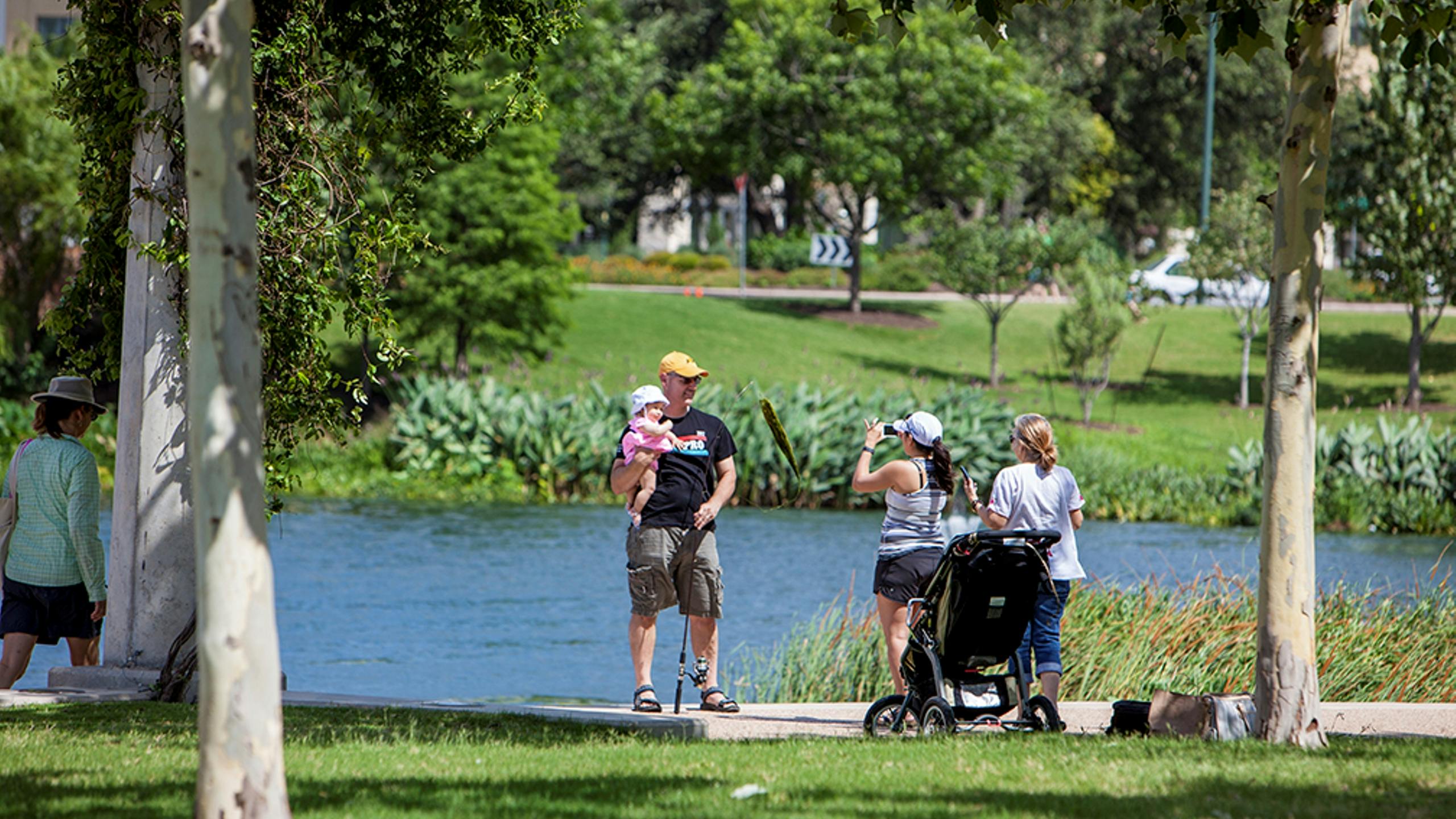 Family taking a photo alongside a lake surrounded by grass and trees at Mueller Lake