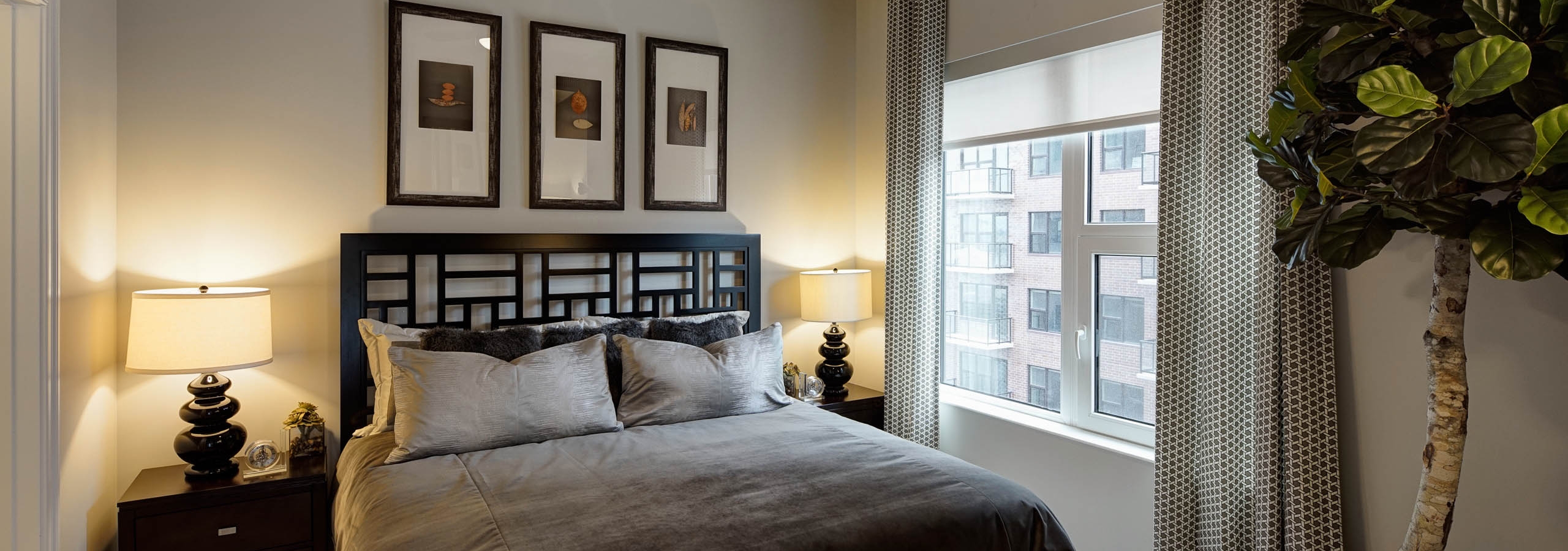 Bedroom at AMLI Lofts with creme colored walls and black and gray furnishings with a bright window view overlooking the city