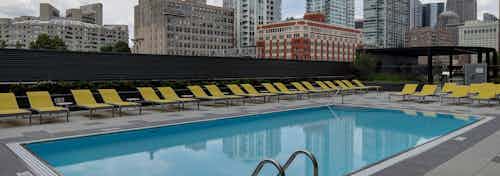 The pool at AMLI Lofts in the daylight with yellow chairs aligning the surrounding pavement and the city skyline in the back