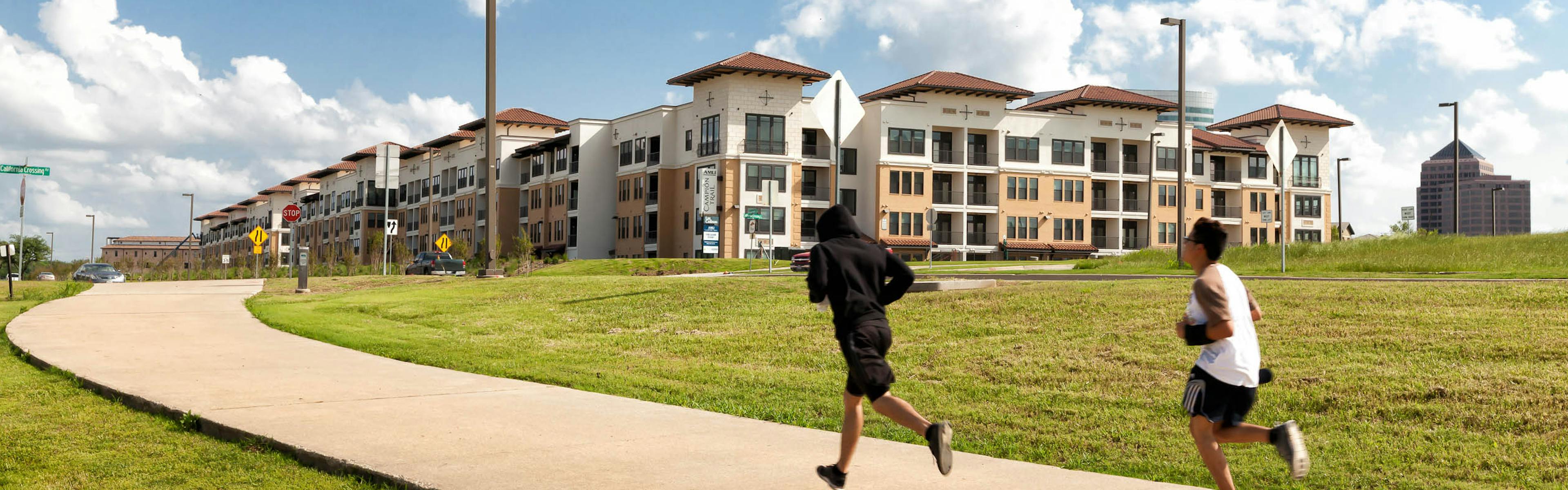 Daytime view of concrete jogging path with joggers and green grass outside of AMLI Campion Trail apartment building