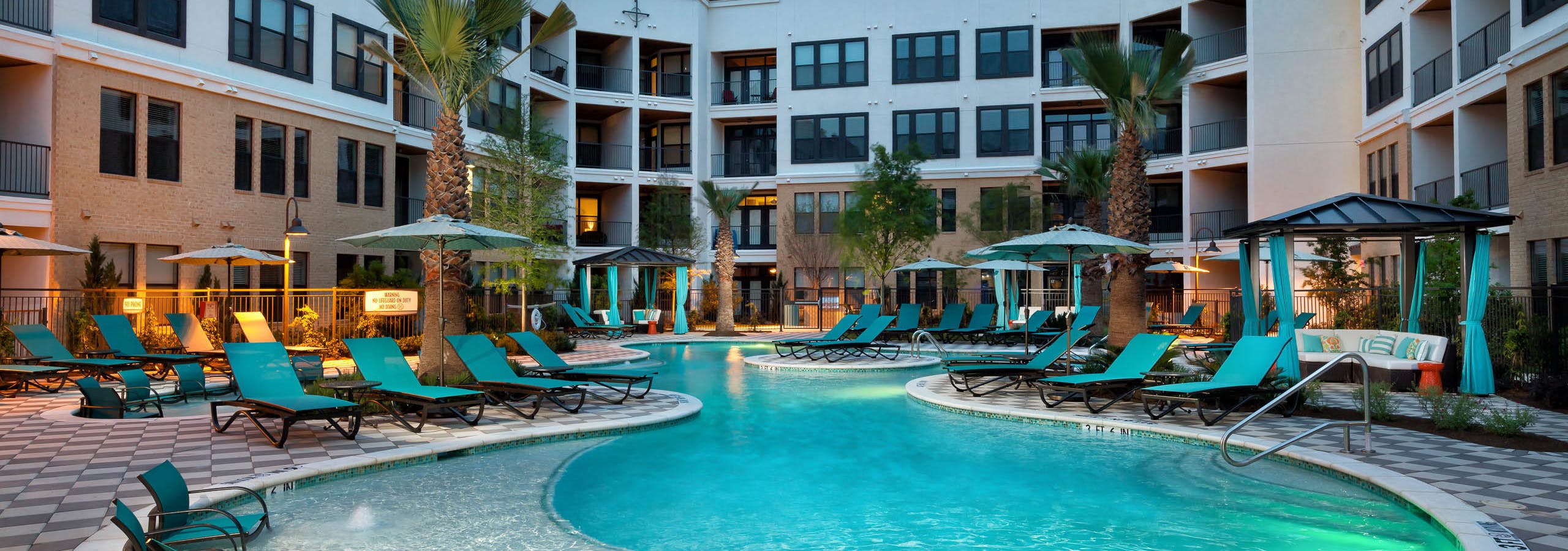 Nighttime view of AMLI Campion Trail courtyard swimming pool with lounge seating and cabanas and umbrellas and palm trees