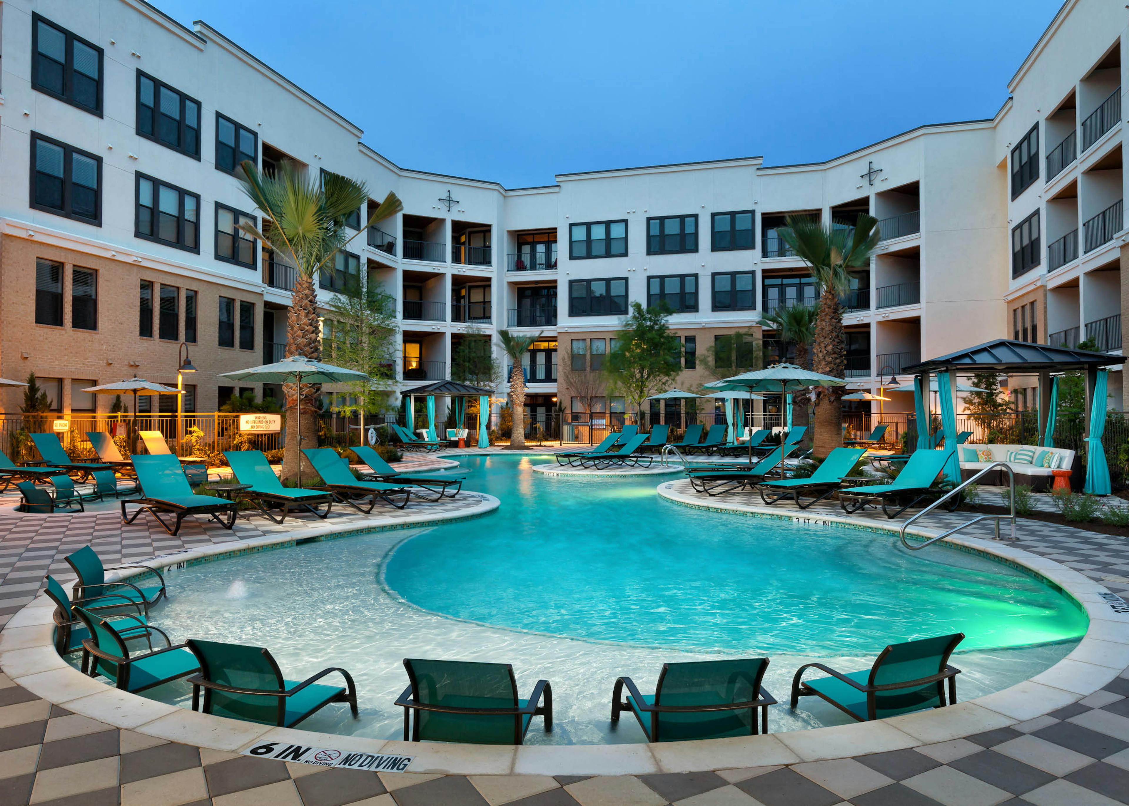 Nighttime view of AMLI Campion Trail courtyard swimming pool with lounge seating and cabanas and umbrellas and palm trees