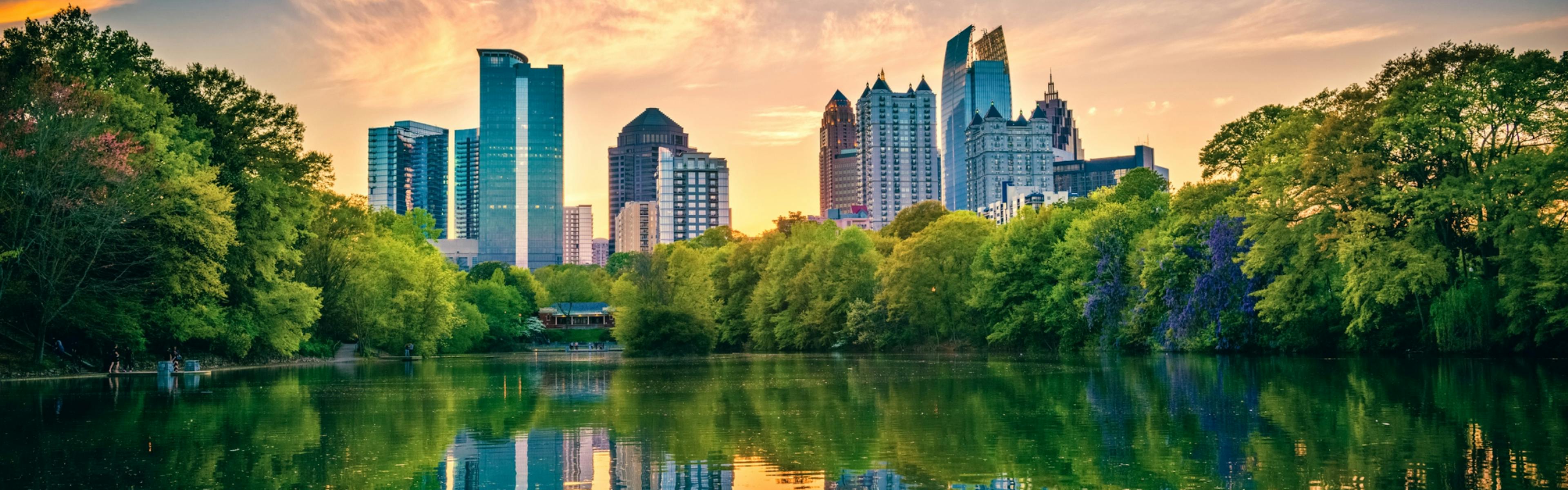 View at down of Atlanta Midtown skyline reflected in a lush tree lined lake with wispy orange clouds