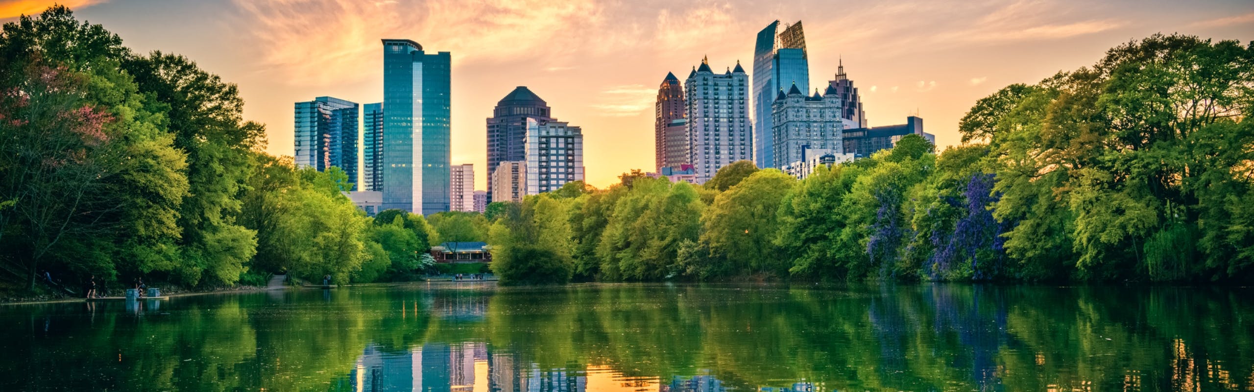 View at down of Atlanta Midtown skyline reflected in a lush tree lined lake with wispy orange clouds