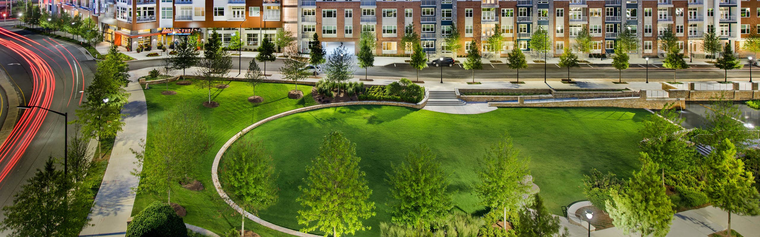 Vibrant grass area with trees and pristine landscaping at AMLI Buckhead with nearby road and building facade in background